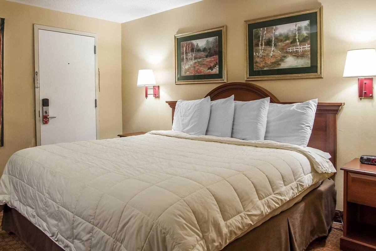 Habitación de hotel con una cama grande, dos lámparas de pared y dos cuadros enmarcados sobre la cama.