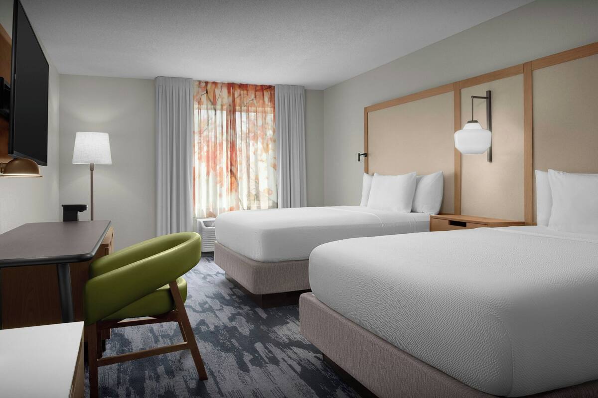 Une chambre d’hôtel avec deux lits, un bureau, une chaise et un téléviseur.