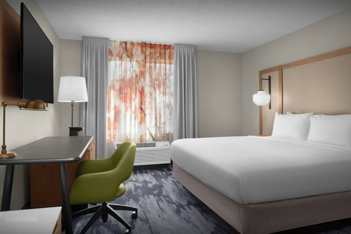 Une chambre d’hôtel équipée d’un lit, d’un bureau, d’une chaise, d’une télévision et d’une fenêtre avec des rideaux.