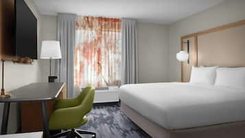 Een hotelkamer met een bed, bureau, stoel, televisie en raam met gordijnen.