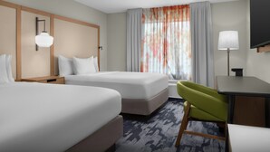 Ein Hotelzimmer mit zwei Betten, einem Schreibtisch, einem Stuhl, einem Fernseher und einem Fenster mit Vorhängen.