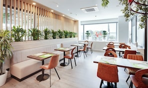 A modern restaurant interior with wooden paneling, green plants, and a mix of seating options including booths and tables.