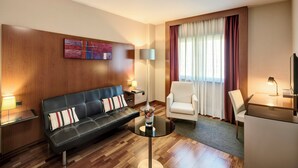 A modern hotel room with a leather sofa, a round glass coffee table, a white armchair, a flat-screen TV, and a large window with curtains. - Hotel Sercotel AB Rivas (Rivas-Vaciamadrid)