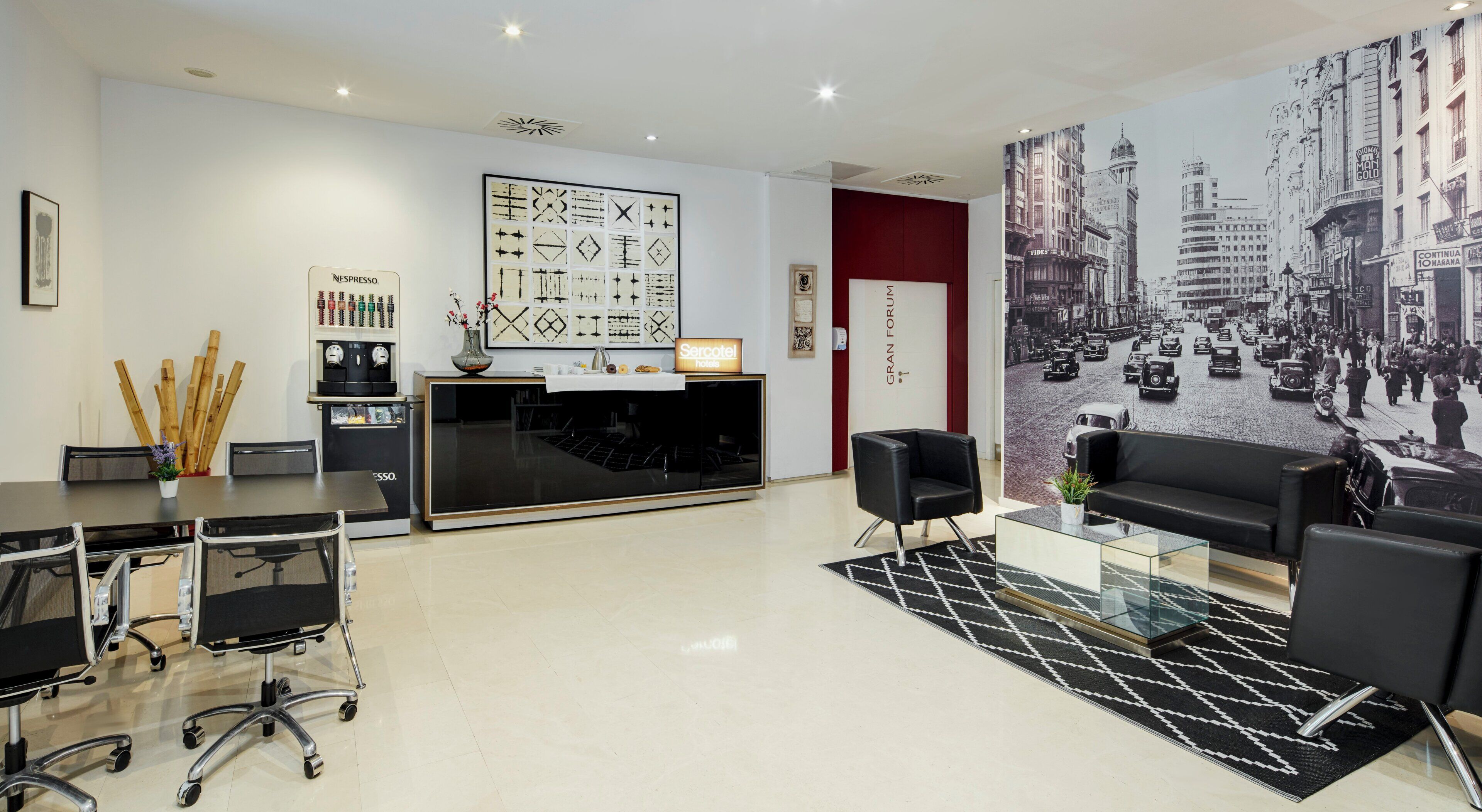 A modern hotel lobby with a reception desk, seating area, and a cityscape mural.