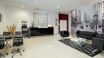 A modern hotel lobby with a reception desk, seating area, and a cityscape mural.