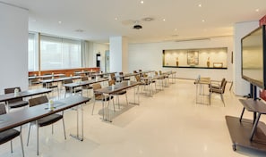 Une salle de conférence équipée de plusieurs tables et chaises, d’un projecteur et d’un grand écran.