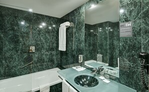 Un bagno moderno con lavabo in vetro, vasca e pareti in marmo.