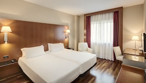 Una habitación de hotel con una cama grande, dos mesitas de noche, un escritorio con una silla, un televisor y una ventana con cortinas.