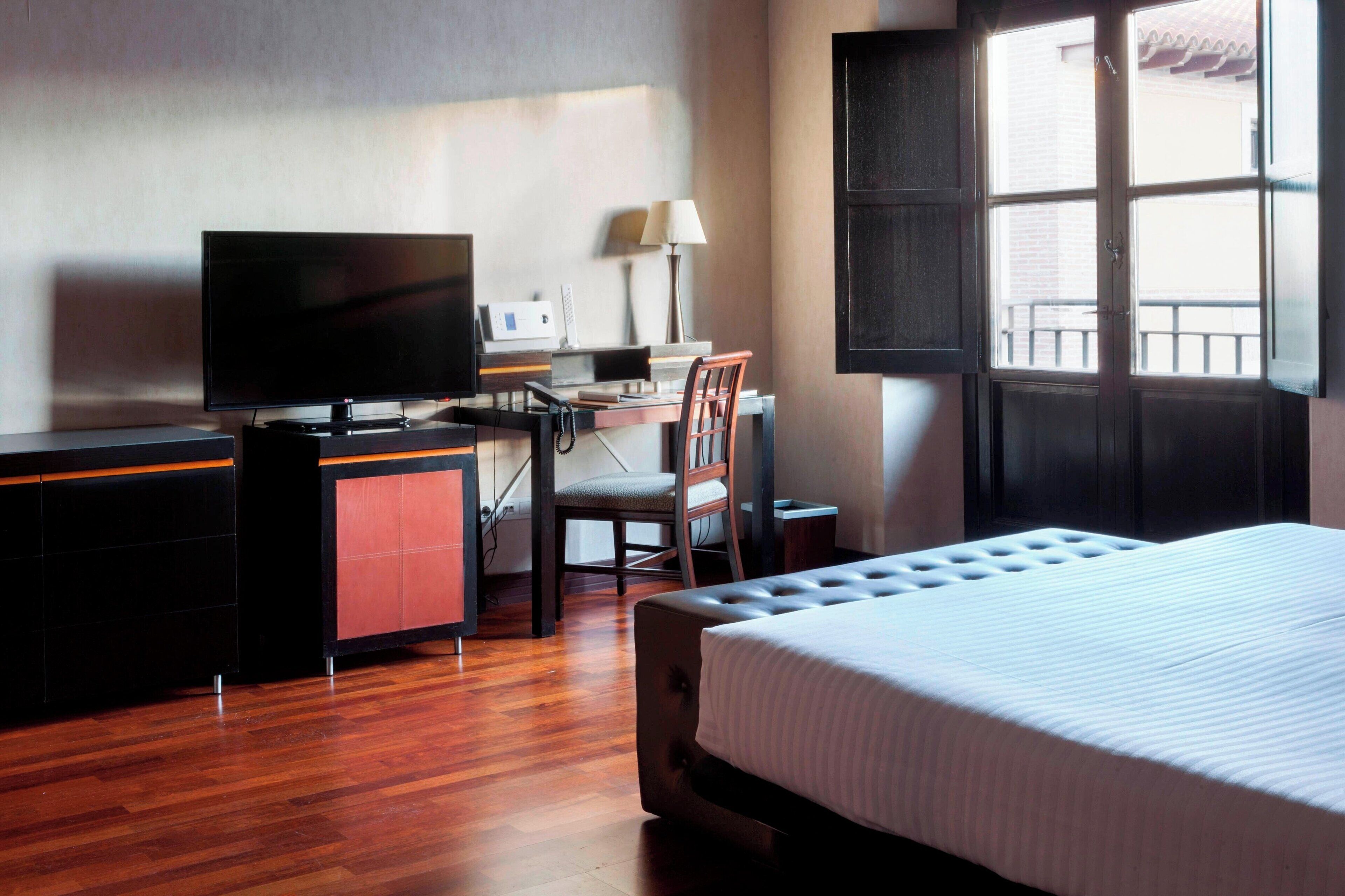 A hotel room with a bed, a desk with a computer, a chair, and a television.