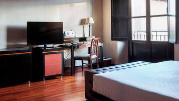 A hotel room with a bed, a desk with a computer, a chair, and a television.