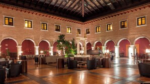 Eine geräumige Lobby mit hoher Decke, Backsteinwänden und mehreren Bögen. Es gibt mehrere Sitzbereiche mit Sofas und Tischen.