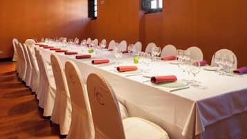 Una larga mesa de conferencias con manteles blancos, servilletas rojas y cristalería dispuesta para una reunión.