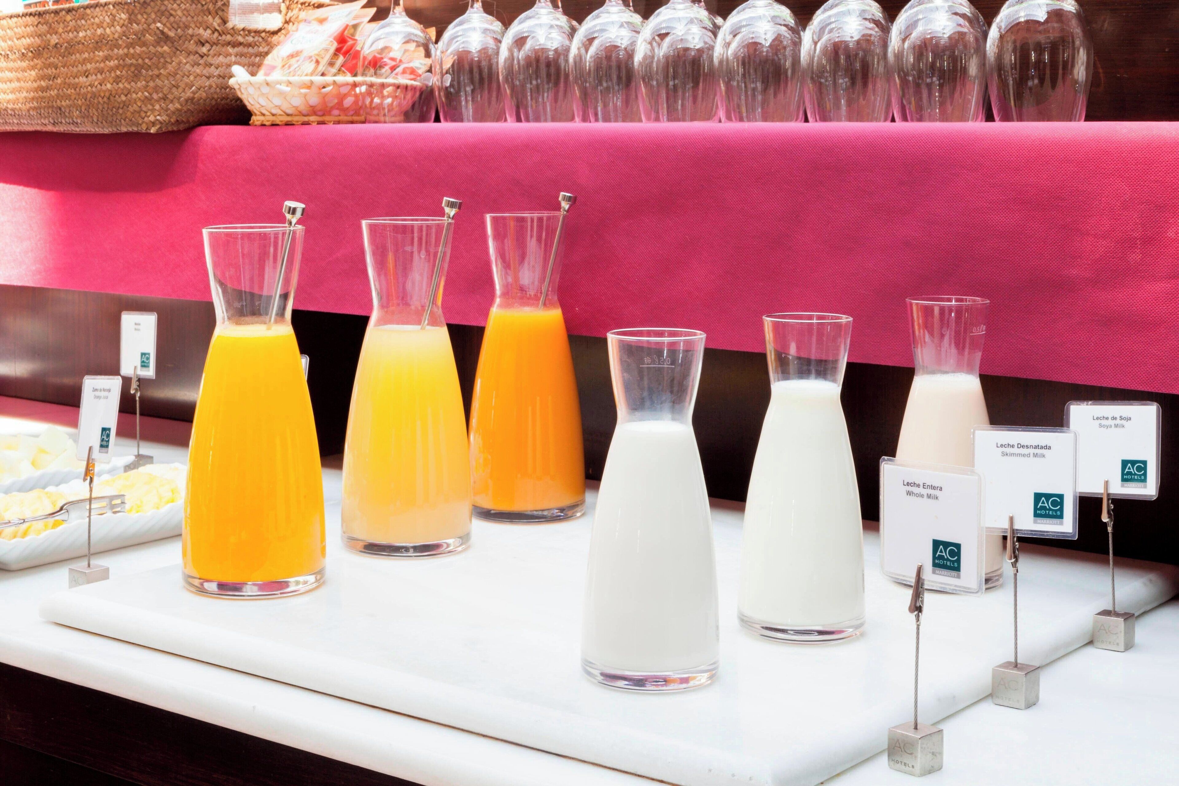 Ein Frühstücksbuffet mit verschiedenen Saft- und Milchsorten, darunter Orangensaft und Vollmilch, präsentiert auf einem Tisch mit rosa Tischdecke.