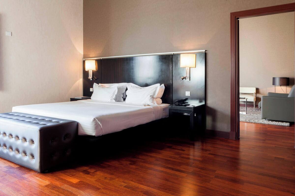 Quarto de hotel com uma cama grande, piso de madeira e duas luminárias de cabeceira.