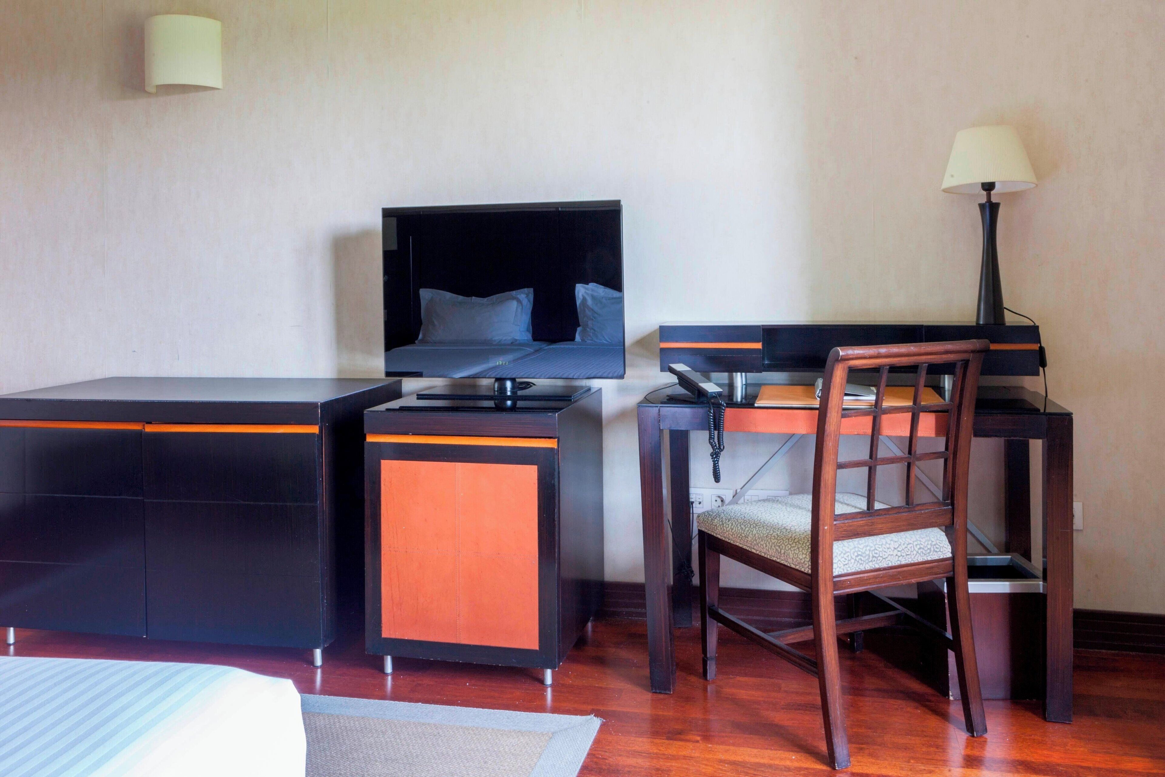 A hotel room with a bed, a desk with a chair, a lamp, and a television.