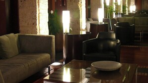 Eine großzügige Lobby mit Backsteinwand, Rundbögen und verschiedenen Sitzbereichen, darunter Sofas und Tische.