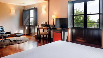 Una habitación de hotel con cama, escritorio con silla, sofá, lámpara y un ventanal con vistas.