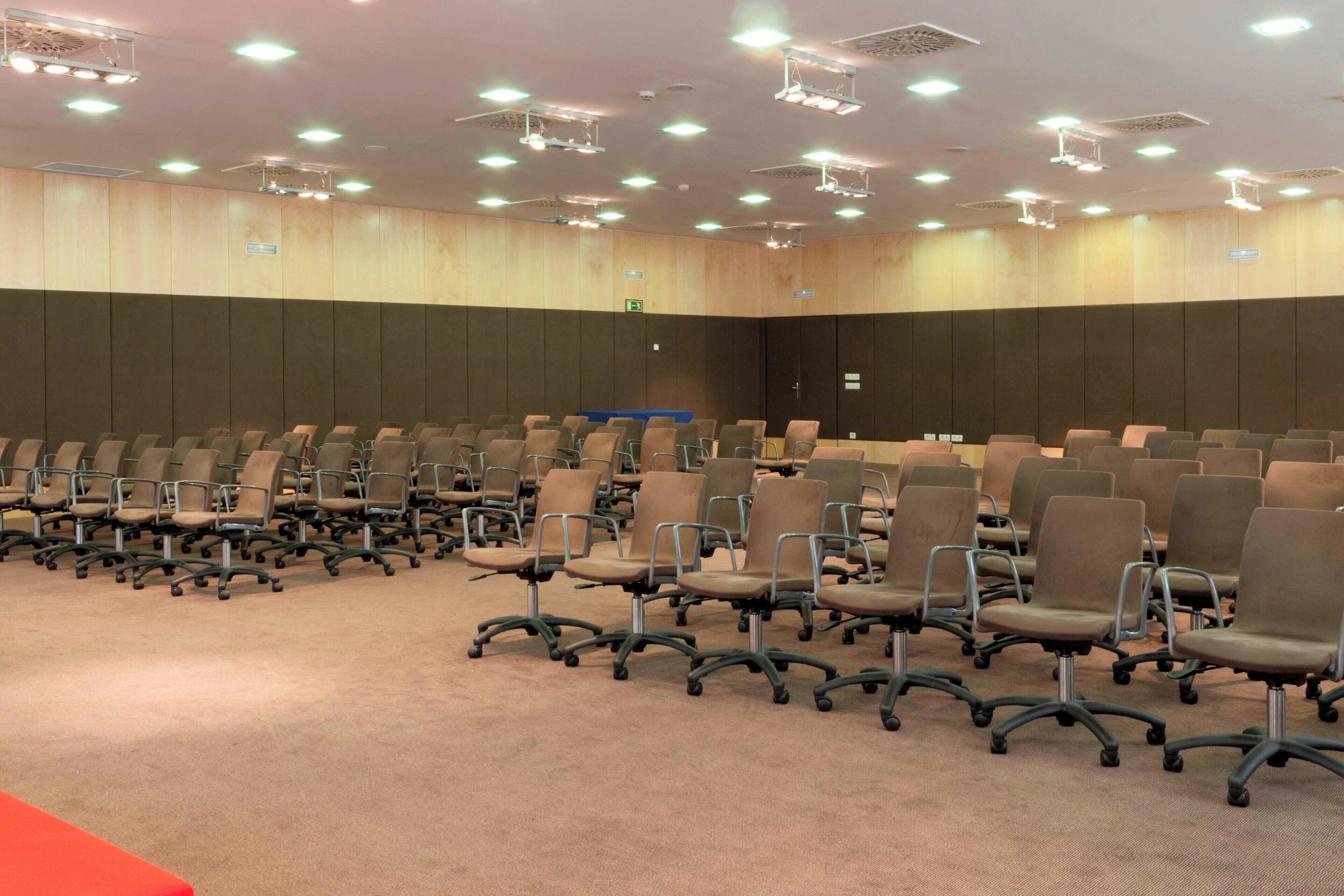 A conference room with rows of chairs, a carpeted floor, and ceiling lights.