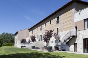 Un edificio de varios pisos con fachada de piedra, una escalera y un césped bien cuidado.