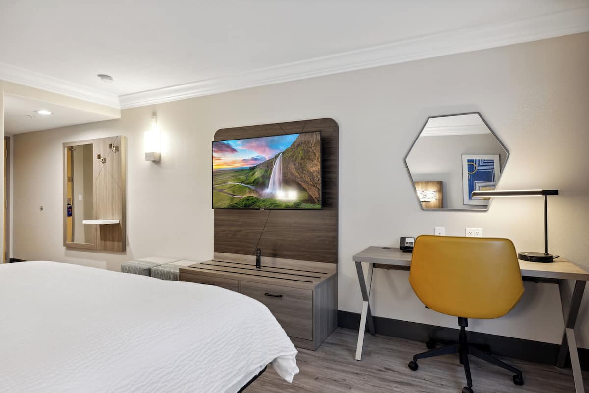 Ein Hotelzimmer mit einem großen Bett, einem Schreibtisch mit Stuhl, einem an der Wand befestigten Fernseher und einem Badezimmer mit Dusche und Toilette.