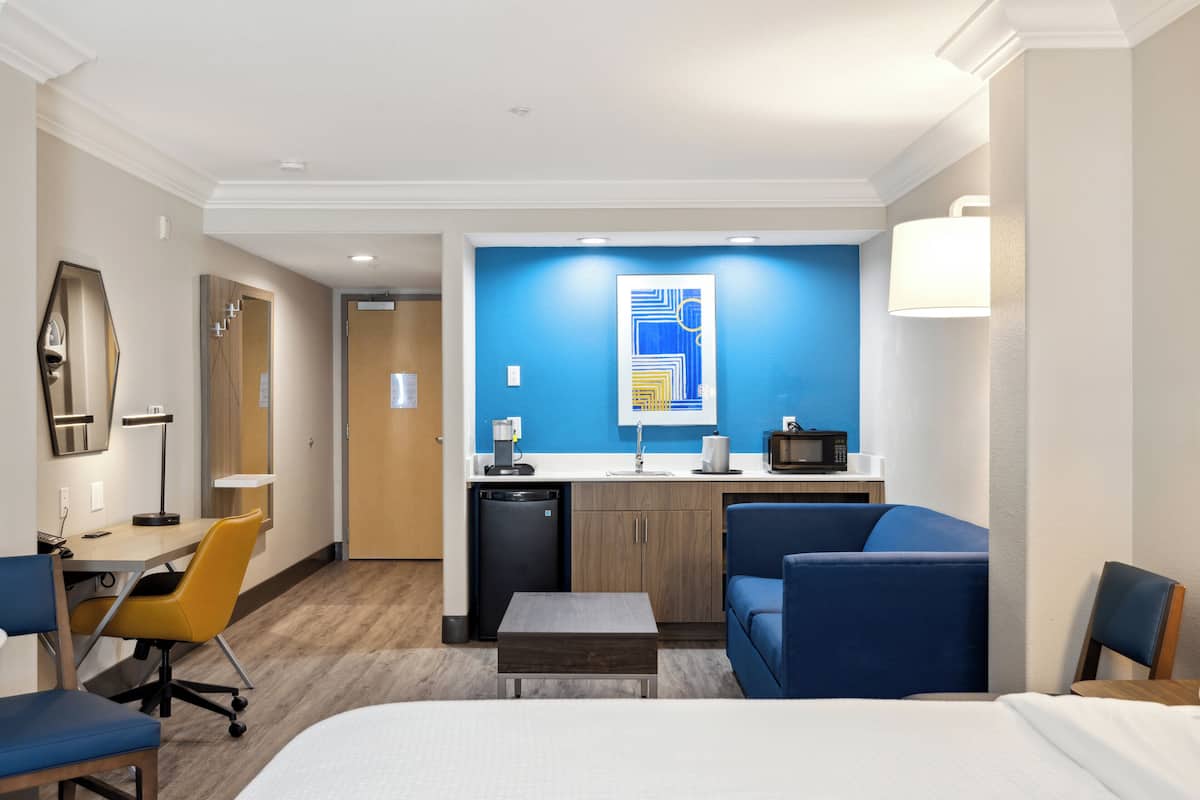Ein Hotelzimmer mit einem Bett, einem Schreibtisch mit Stuhl, einer Couch, einem kleinen Tisch, einer Mikrowelle, einem Waschbecken und einem Schrank.