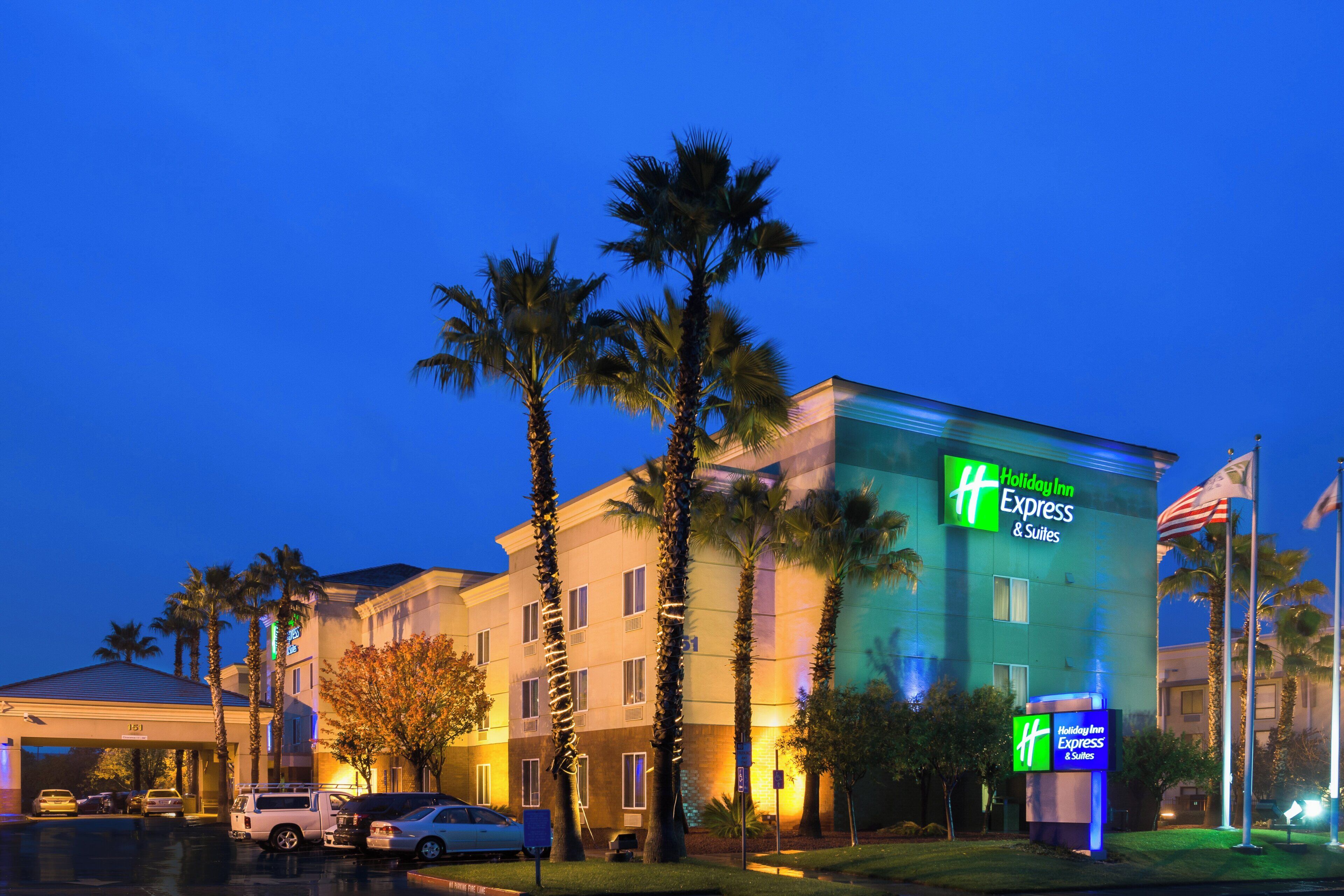 A Holiday Inn Express building with a sign, palm trees, and parked cars.