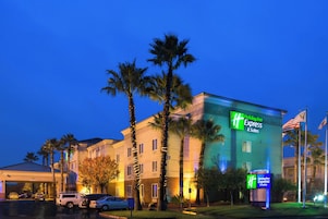 Edificio de Holiday Inn Express con letrero, palmeras y coches estacionados.