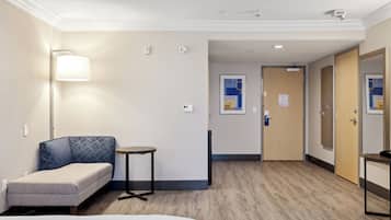 Una habitación de hotel con cama, sofá, una mesita, una lámpara y una puerta que da a otra habitación.