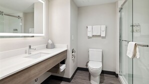 A modern bathroom with a white sink, wooden vanity, a toilet, and a glass shower enclosure. - Holiday Inn Express Hotel & Suites Vacaville by IHG (Vacaville)