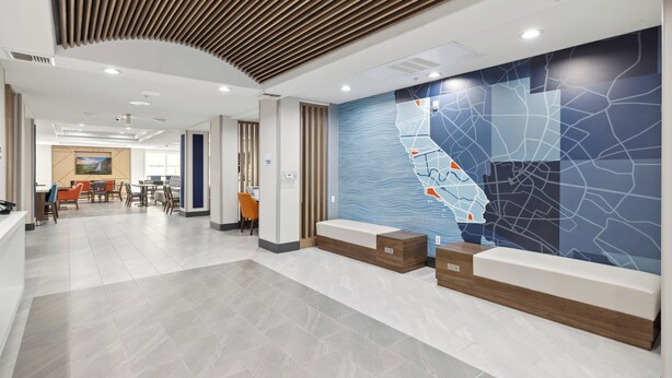A modern hotel lobby with a reception desk, seating area, and a large wall mural. - Holiday Inn Express Hotel & Suites Vacaville by IHG (Vacaville)