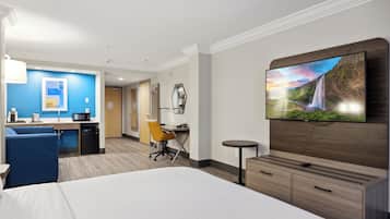 Una habitación de hotel con una cama grande, un escritorio con una silla, una mesita y un televisor montado en la pared.