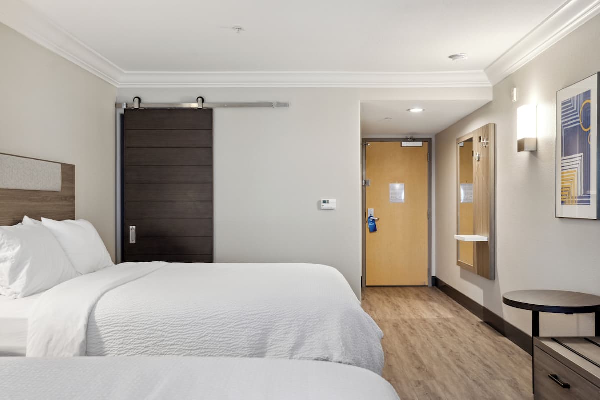 Ein Hotelzimmer mit zwei Betten, einer Holztür, einem kleinen Tisch und einer Wandleuchte.
