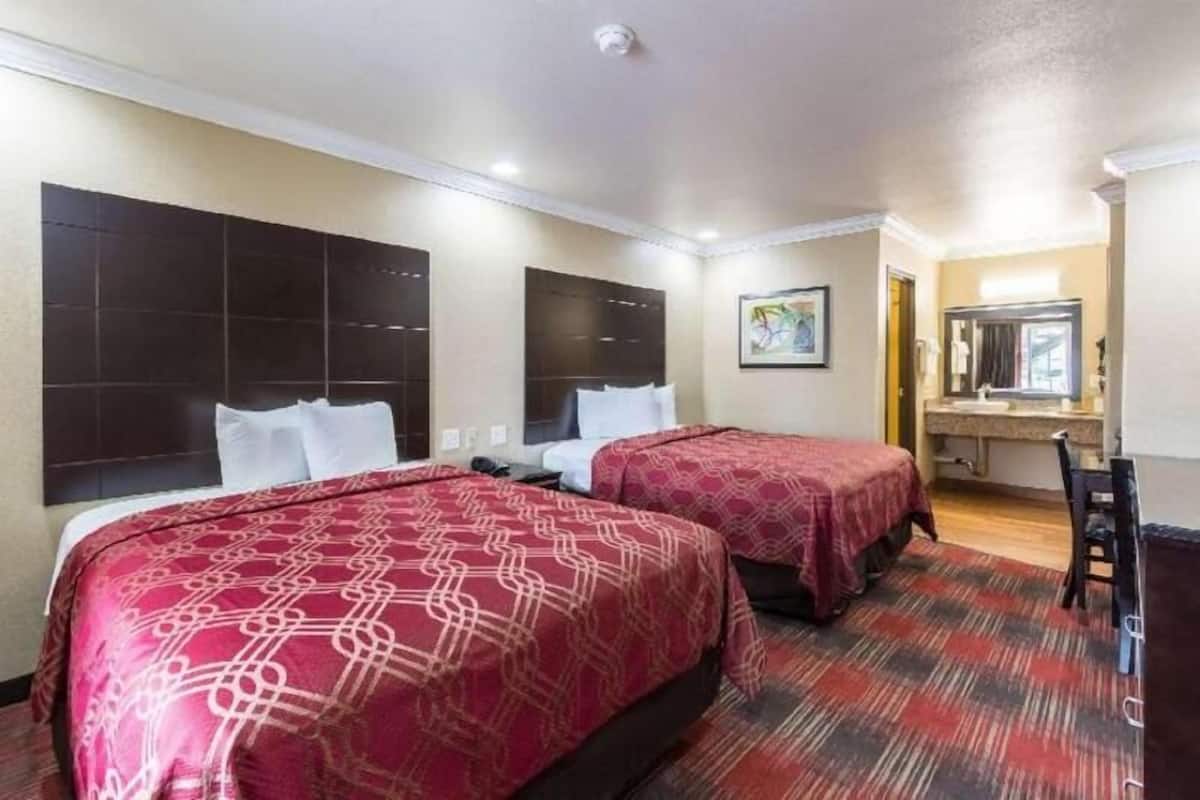 Une chambre d’hôtel avec deux lits, un bureau, une chaise et une salle de bain visible à travers une porte ouverte.