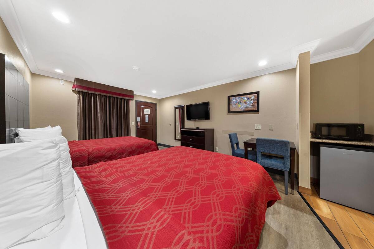 Une chambre d’hôtel avec deux lits, un bureau, une chaise, une télévision et un four à micro-ondes.