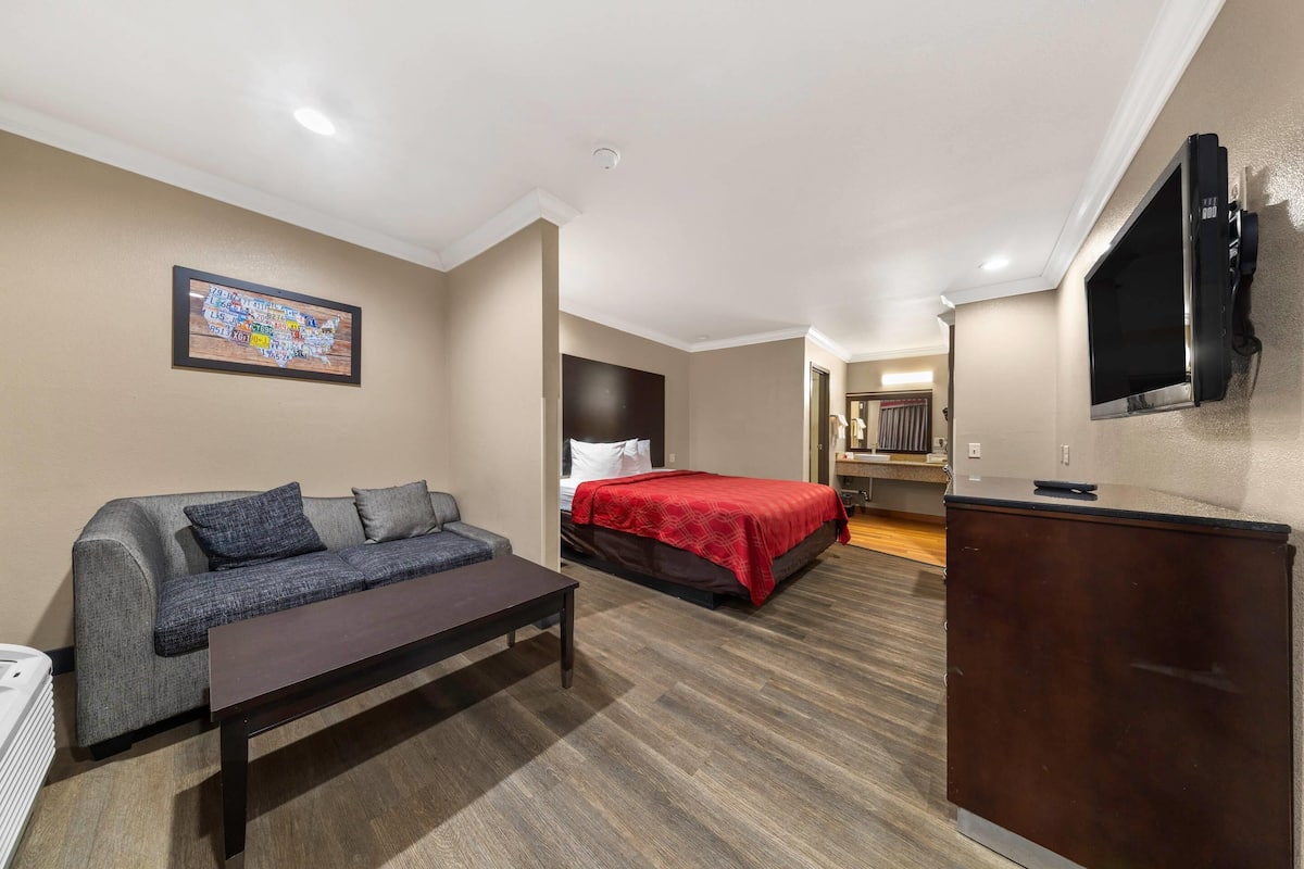 Une chambre d’hôtel avec un canapé, un lit recouvert d’une couverture rouge, un téléviseur fixé au mur et un bureau.
