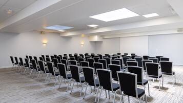 Un salón de conferencias con filas de sillas, techo blanco e iluminación empotrada.
