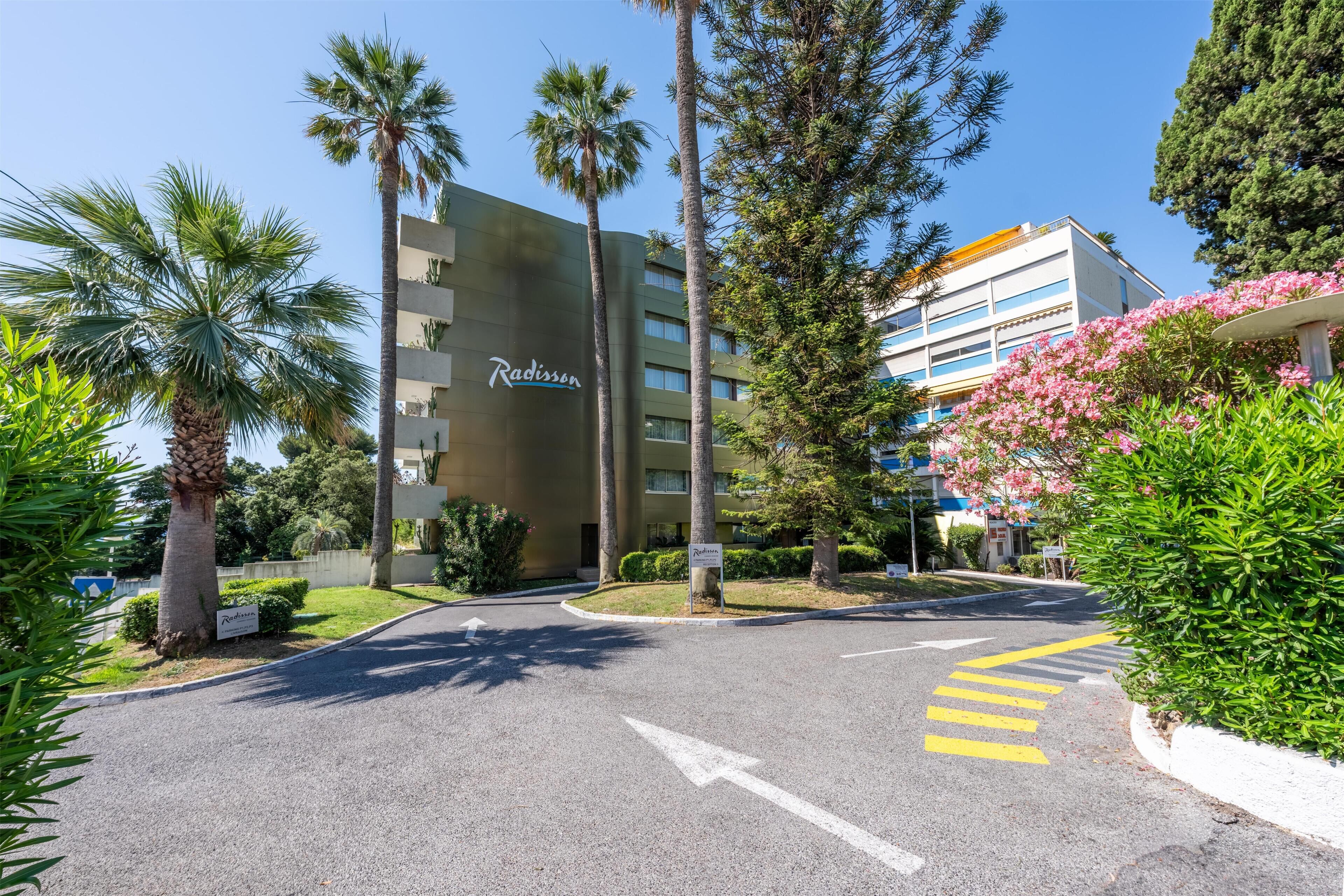 Een hotelentree met palmbomen, een bord waarop 'Radisson' staat en een weg met pijlen.