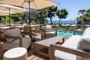 Una terraza con mobiliario exterior, una piscina y vista al mar.