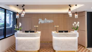Un mostrador de recepción con encimera de mármol y base dorada, dos lámparas colgantes y una pared de madera con el nombre 'Radisson' en el centro.
