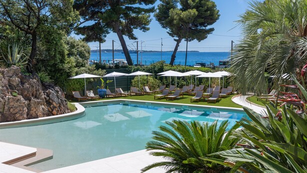 A swimming pool with lounge chairs and umbrellas, surrounded by trees and a view of the sea. - Radisson Hotel Cannes Seaside (Cannes)