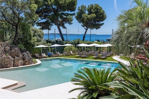 A swimming pool with lounge chairs and umbrellas, surrounded by trees and a view of the sea. - Radisson Hotel Cannes Seaside (Cannes)