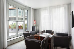 A modern hotel room with a large window, a dining table with chairs, a flat-screen TV, and a small cabinet. - Sina The Gray (Milan)