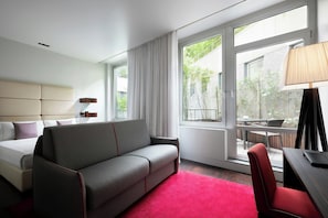 A hotel room with a bed, a sofa, a desk, a chair, and large windows. - Sina The Gray (Milan)