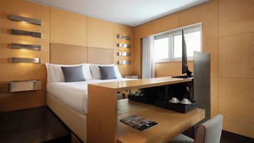Una habitación de hotel moderna con una cama, paneles de madera, un escritorio con cafetera y una ventana.