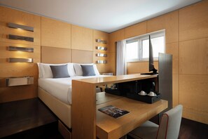 Quarto de hotel moderno com uma cama, painéis de madeira, uma mesa com cafeteira e uma janela.