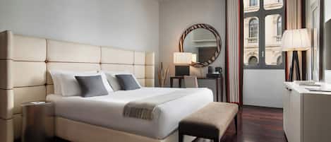 A hotel room with a large bed, bedside tables, a desk, a chair, a mirror, and a view of buildings through a window.