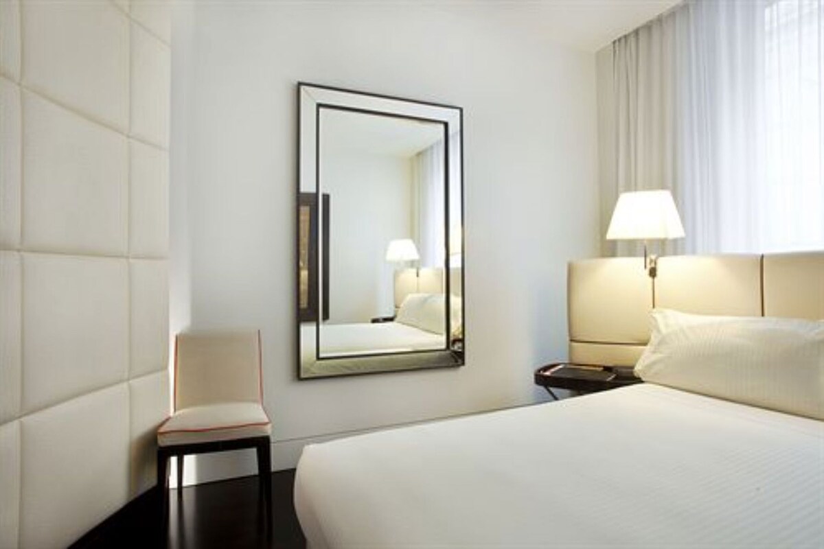 A hotel room with a large bed, a chair, a nightstand, a lamp, and a mirror.