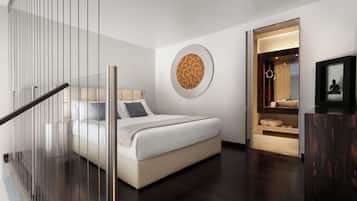 Un dormitorio moderno con cama, barandilla de vidrio, una obra de arte en la pared y un estante empotrado con toallas.