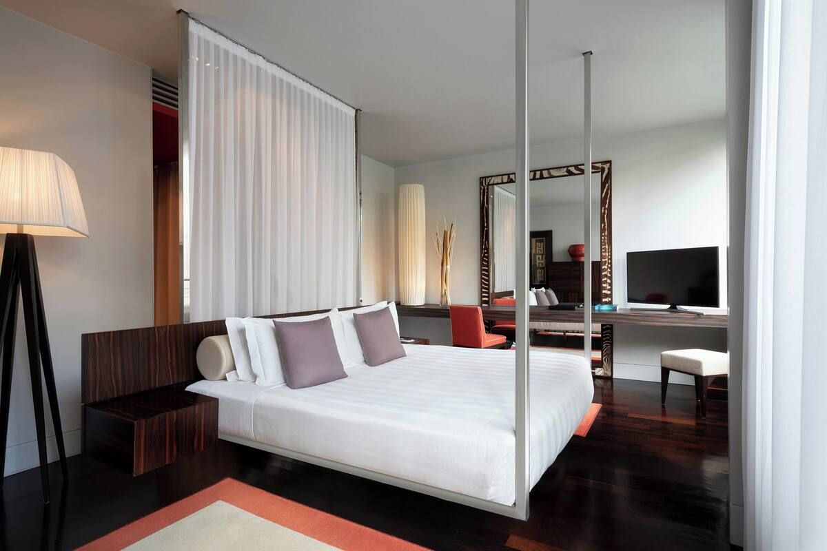 A modern hotel room with a large bed, a desk, a chair, a TV, and a large mirror.