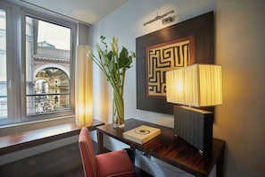 A hotel room with a view of a historic building, a desk with a lamp, a vase with flowers, and a framed geometric artwork. - Sina The Gray (Milan)